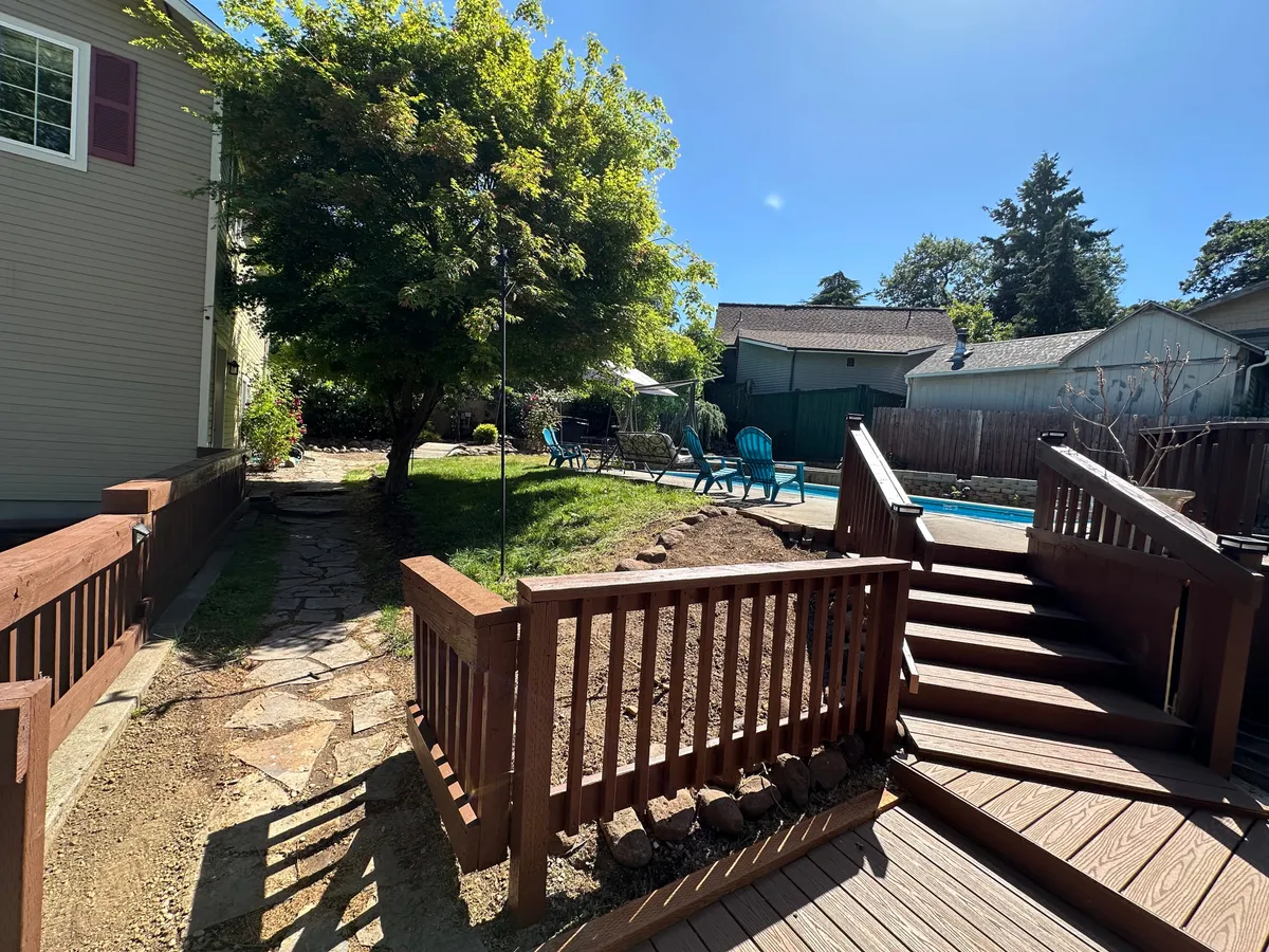 A broad view of the condo community’s pool area, featuring a sun-drenched deck with Adirondack chairs, lush green surroundings, and a fire pit area. The atmosphere is calm yet social, ideal for relaxed outdoor living.