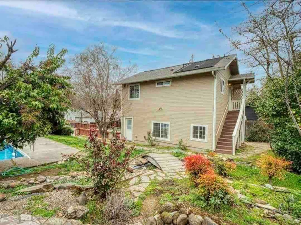 The image showcases the condo’s charming exterior framed by lush garden plants, a stone pathway leading to the entrance, and a sparkling swimming pool set in a tranquil, sun-dappled setting. The atmosphere is peaceful, inviting guests to relax outdoors, enjoy a swim, or savor quiet moments in the garden.
