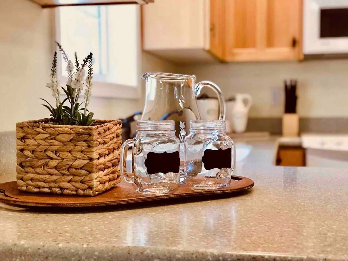 A small, cozy dining nook set with a glass pitcher, mason jars, and a woven planter. The soft, natural light and thoughtful tableware invite relaxed brunches or a quiet cup of tea, fostering a sense of comfort and connection.