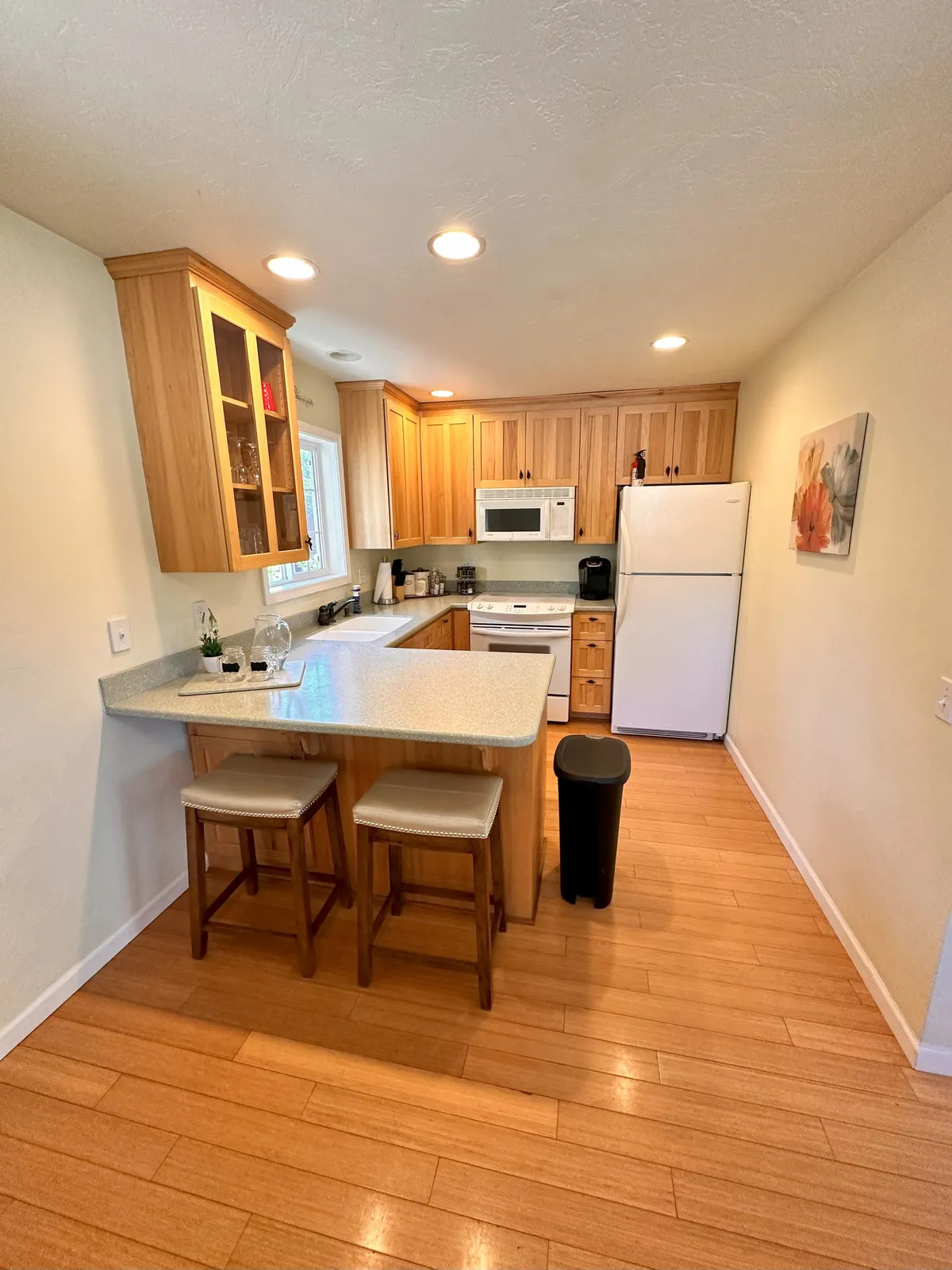 A welcoming kitchen scene with a kitchen island, stools, wooden cabinets, visible appliances, and decorative touches like artwork. The space feels perfect for intimate breakfasts, casual snacks, or preparing a romantic dinner.