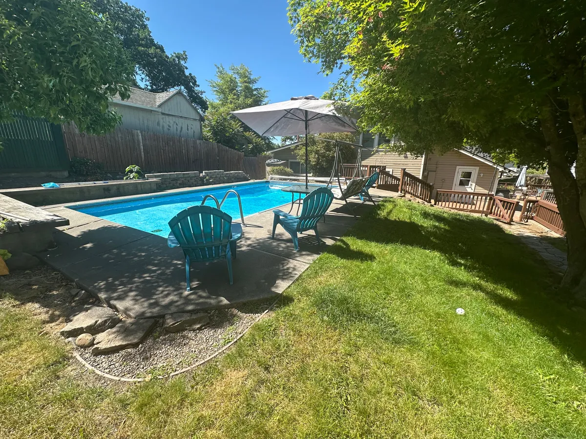 A tranquil poolside scene with lounge chairs, a shady umbrella, and vibrant greenery. Steam rises from the water in the gentle morning sun, suggesting a peaceful start to the day with coffee by the pool.