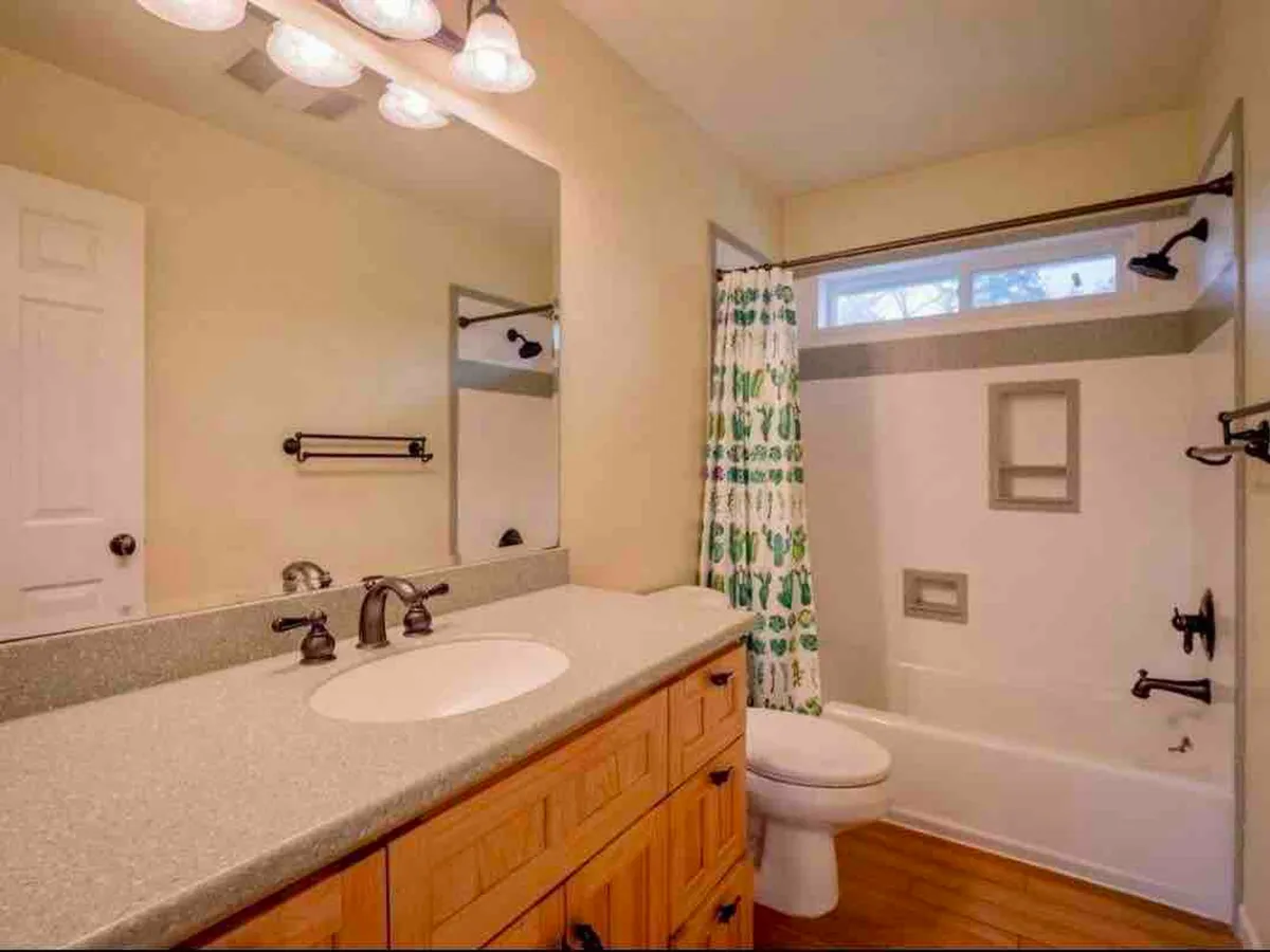 A fresh and inviting bathroom featuring a vanity with sink, a bathtub with an overhead shower, and a decorative shower curtain. The space is clean and well-lit, with modern fixtures and thoughtful touches like fresh towels.