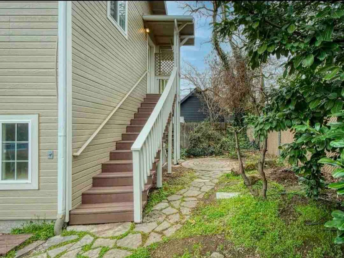This image shows the exterior of a home with stairs leading up to the entrance, surrounded by lush greenery and a peaceful stone pathway. The scene exudes a tranquil, inviting atmosphere, perfect for a couple's quiet arrival or departure.